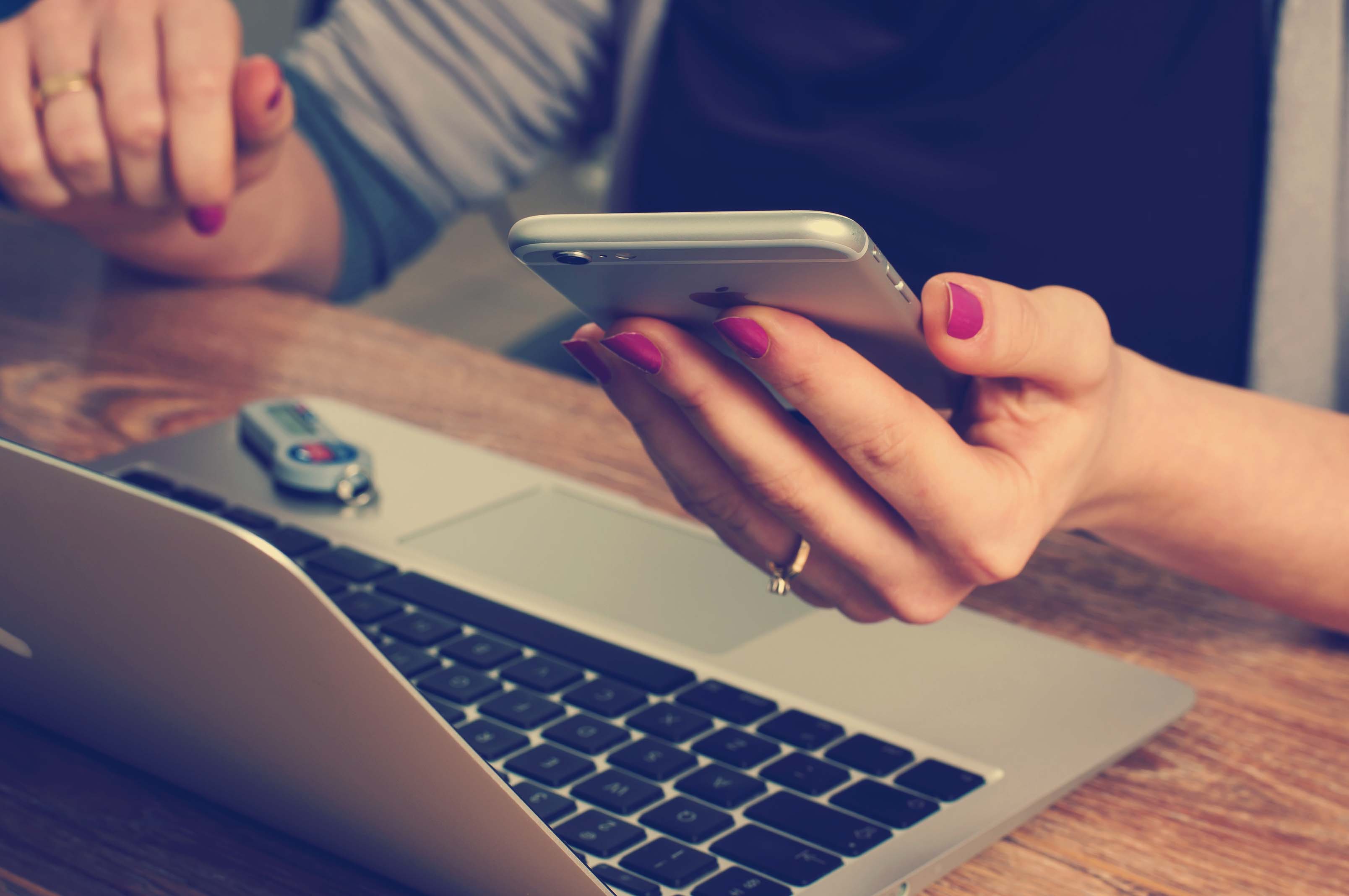 Woman on an iPhone using a laptop.