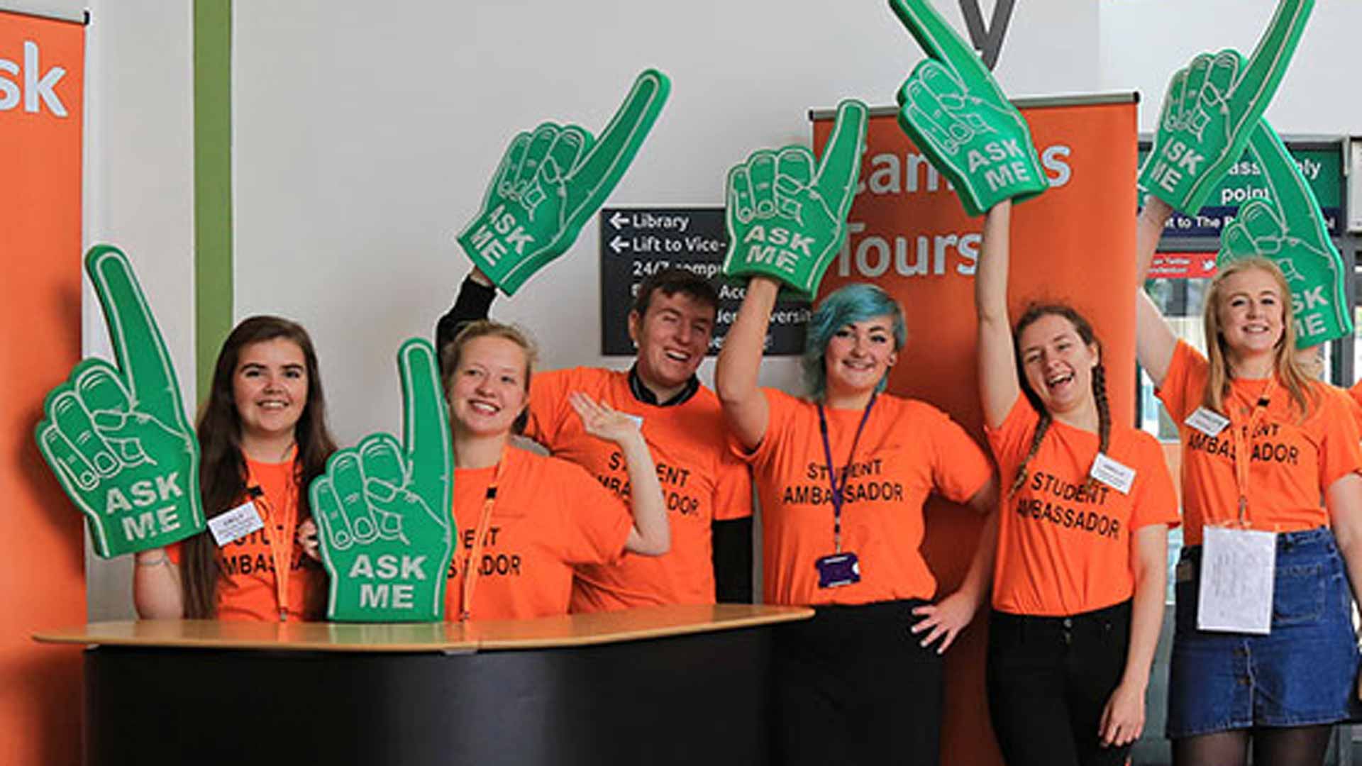 Open Days student ambassadors with 'Ask me' gloves on pointing up in the air.