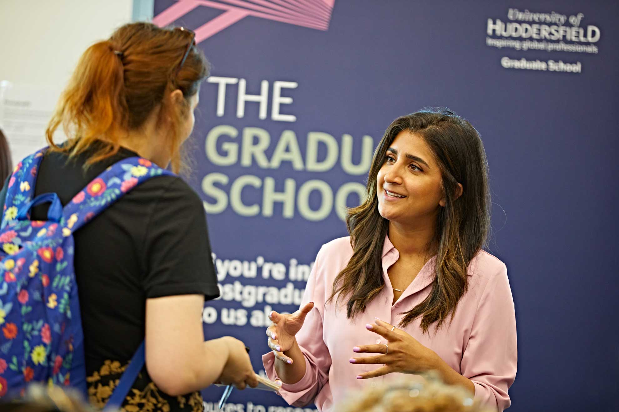 two people talking in front of a grad school banner