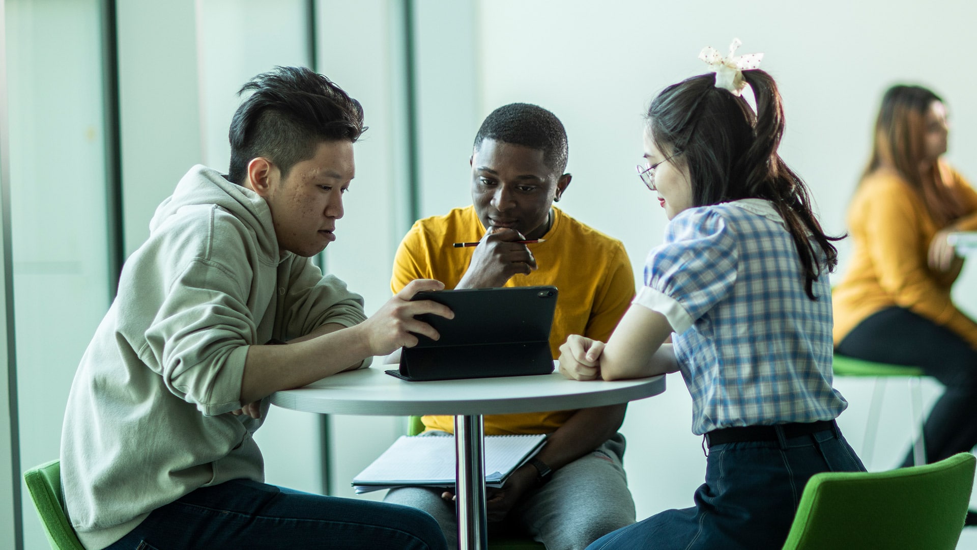 Three students sat at a table looking curiously at a tablet device.
